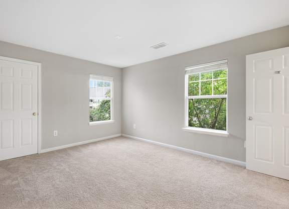 A room with two windows and carpeted flooring.