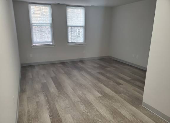 A room with wooden flooring and two windows.