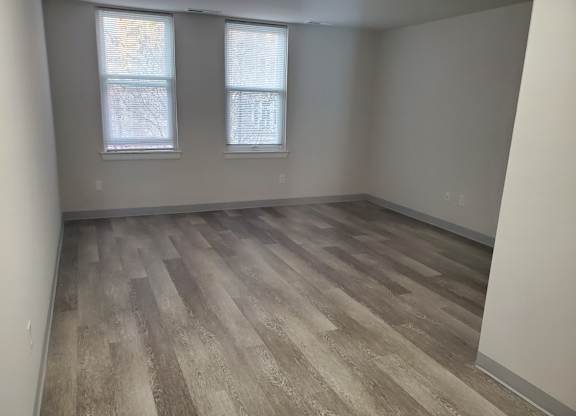 A room with wooden flooring and two windows.