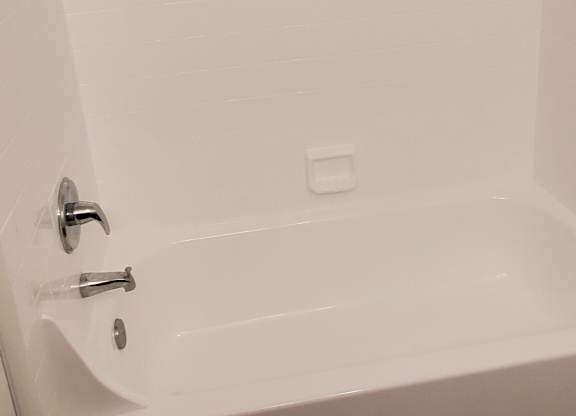 A white bathtub with a shower head and two faucets.