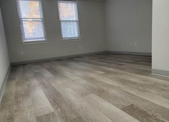 A room with wooden flooring and two windows.