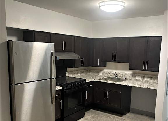 A kitchen with a stainless steel refrigerator and black cabinets.