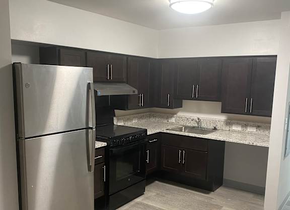 A stainless steel refrigerator in a kitchen with a curtain hanging in the background.