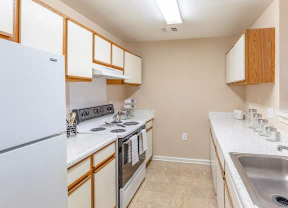 A kitchen with a white refrigerator, stove, and sink.