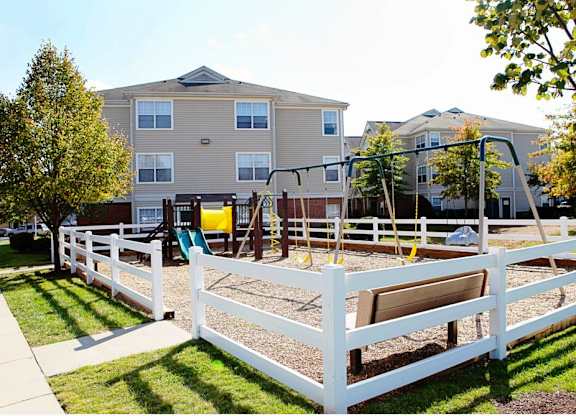 A playground with a white fence and a yellow slide is in front of apartment buildings.