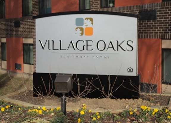 A sign for Village Oaks apartment homes stands in front of a brick building.