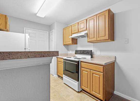A kitchen with a stove top oven and wooden cabinets.