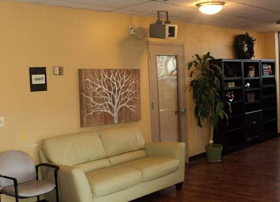 A room with a couch, chair, and a painting of a tree.