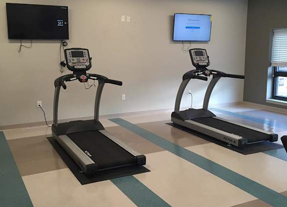 Two treadmills are placed in a room with a TV mounted on the wall.