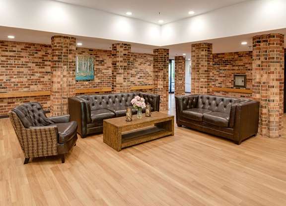 A room with a brick wall and wooden flooring has three black leather sofas.