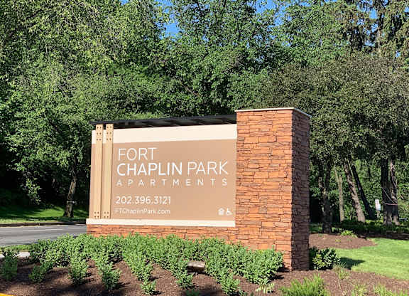 A sign for Fort Chaplin Park Apartments is displayed in front of a green tree.