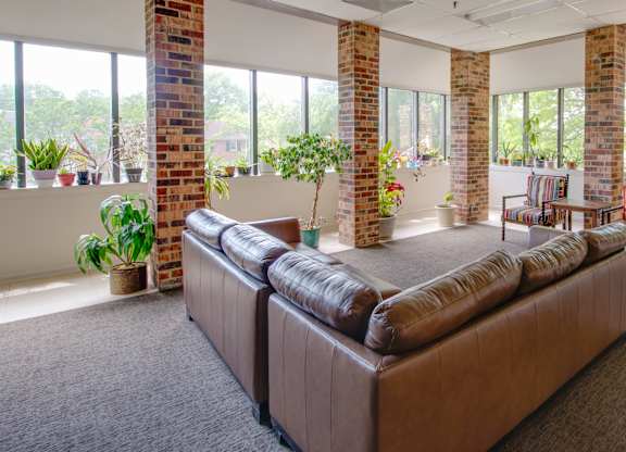 A brown couch in a room with a brick wall and a carpet.