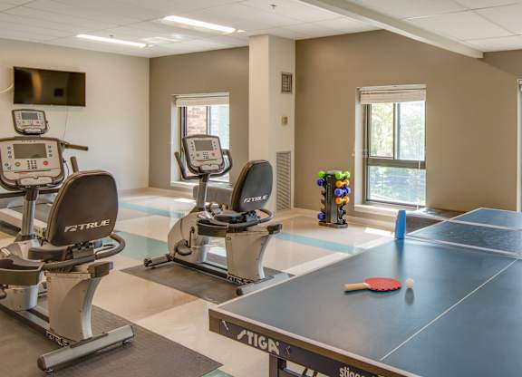 A ping pong table is in the middle of a gym with treadmills and exercise bikes.