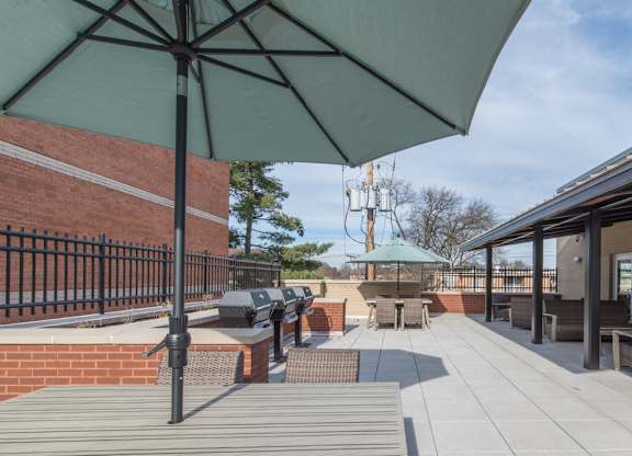 A patio with a green umbrella and a brick wall.