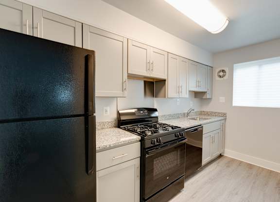 A black refrigerator sits in a kitchen with white cabinets.