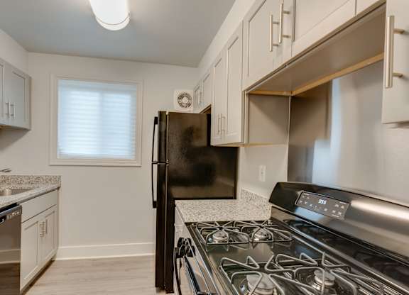 A kitchen with a black refrigerator, stove, and white cabinets.
