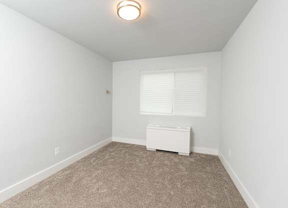 A room with a carpeted floor and a window with blinds.