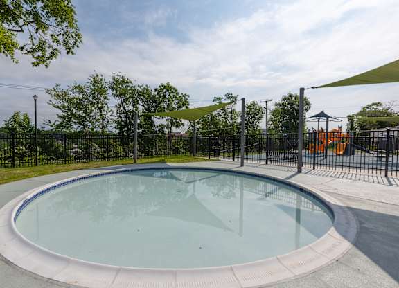 A round glass pool surrounded by a black fence with trees in the background.
