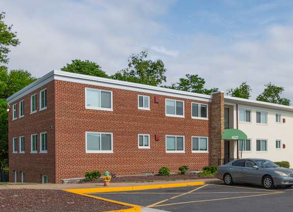A parking lot in front of a red brick building with a white building in the background.