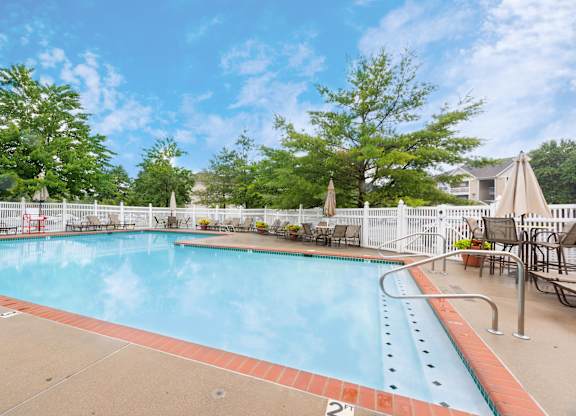 A large outdoor swimming pool surrounded by a white fence and trees.