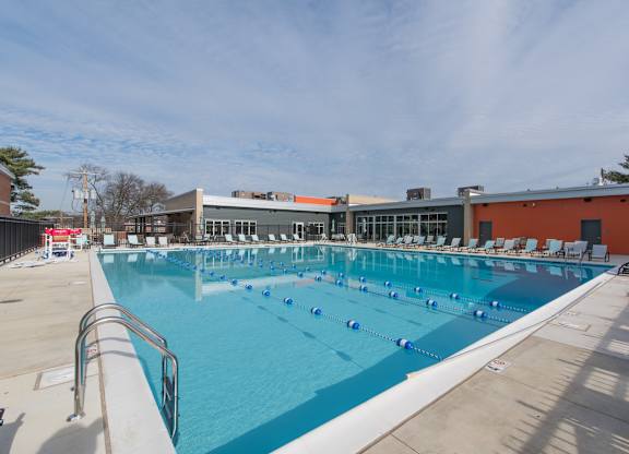 A large outdoor swimming pool with sun loungers and a building in the background.