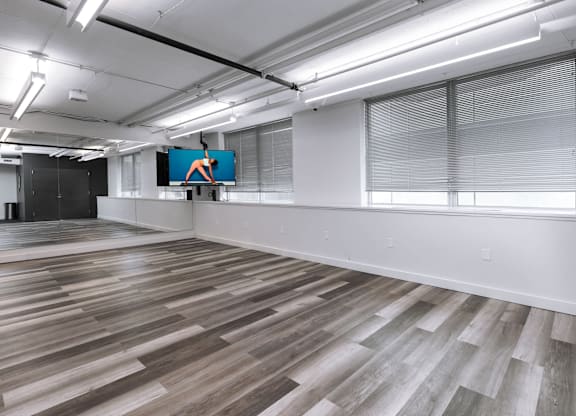 A spacious room with wooden flooring and a large screen displaying an orange figure at Clayton on the Park Apartments, Missouri