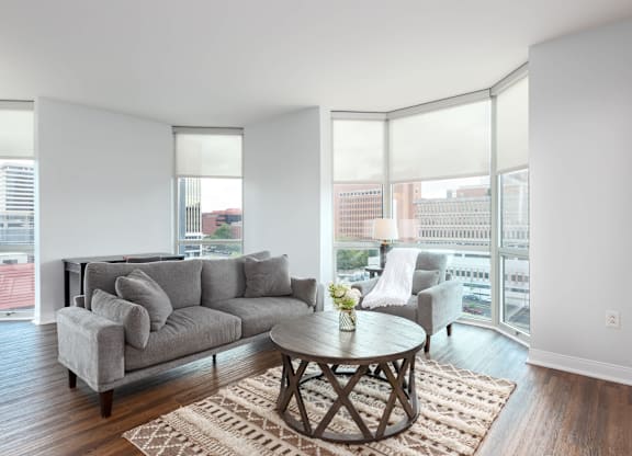 A living room with a grey couch, a coffee table and a large window at Clayton on the Park Apartments, Clayton, MO, 63105
