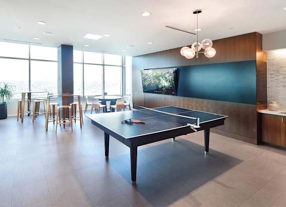 A ping pong table is in the middle of a room with a tv and a bar.