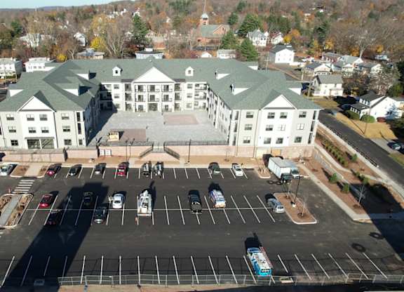 A large white building with a green roof is surrounded by a parking lot.