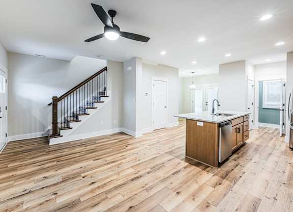 A spacious kitchen with a wooden floor and a staircase with a black railing.