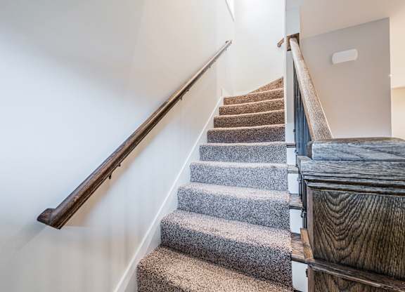 A staircase with a wooden handrail and carpeted steps.