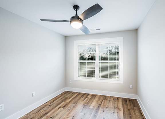 A room with a ceiling fan and a window with blinds.