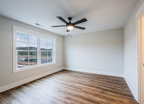 A room with a ceiling fan and a window overlooking a parking lot.