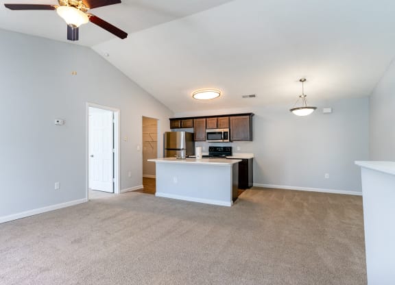 an empty living room with a kitchen and a ceiling fan