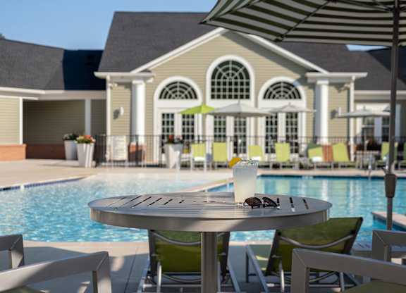 A table with a glass of milkshake and sunglasses on it in front of a pool.