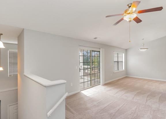 an empty living room with a ceiling fan and a door to a balcony
