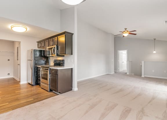 an empty living room with a kitchen and a ceiling fan