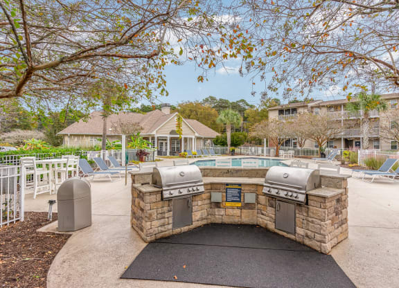 a patio with a grill and a pool with chairs at Litchfield Oaks Apartments, Pawleys Island, SC