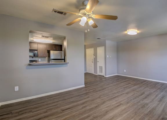 an empty living room with a ceiling fan and a kitchen