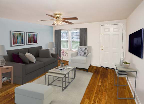 A living room with a grey couch, a coffee table, and a flat screen TV mounted on the wall.