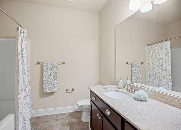 A bathroom with a white sink, toilet, and a bathtub with a white curtain.