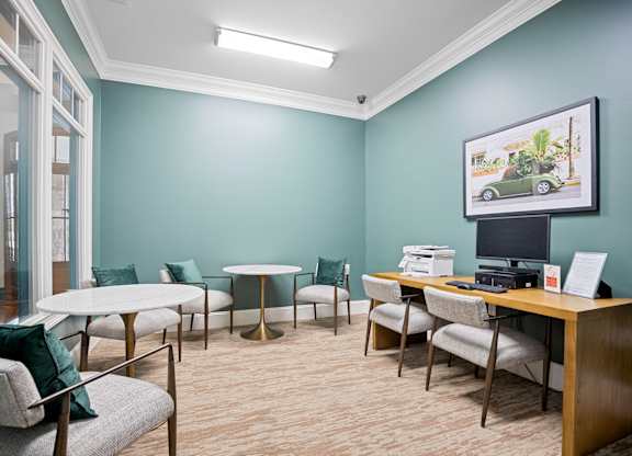 A room with a desk, chairs, and a framed picture of a car on the wall.