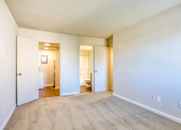 the living room and bedroom of an apartment with carpeting and white walls
