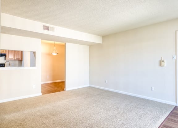 an empty living room with a white door and a kitchen