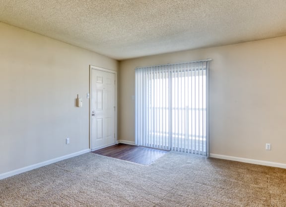 the spacious living room of an apartment with a large window and a door