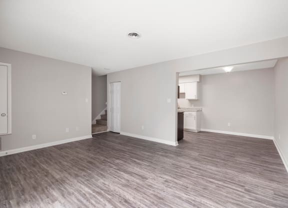 an empty living room with a kitchen in the background