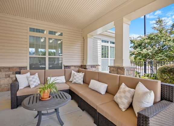 A patio with a couch, pillows and a table.