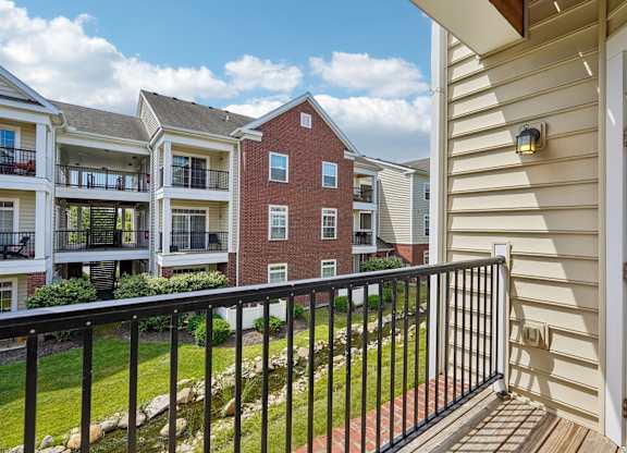 A balcony overlooks a grassy area and a brick building.