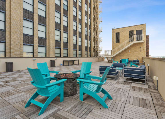 a patio with blue chairs and a fire pit in front of a brick building