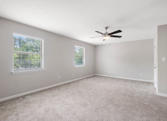 an empty bedroom with a ceiling fan and three windows